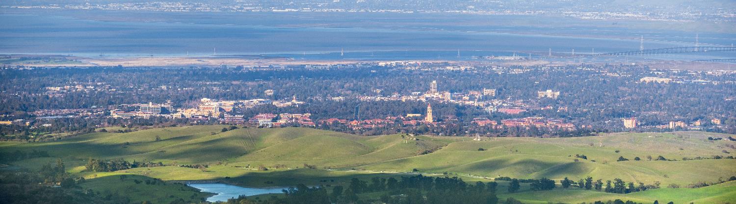 An eastern facing view of the Palo Alto area with rolling green foothills in the foreground to Stanford University, Downtown Palo Alto and surrounding neighborhoods out to the Baylands and across the distant bay.