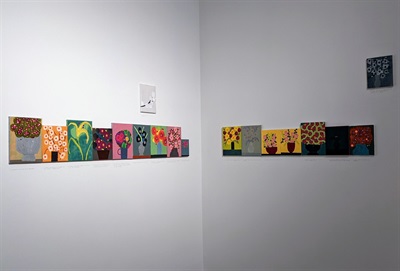A row of small paintings of flowers in the corner of the gallery