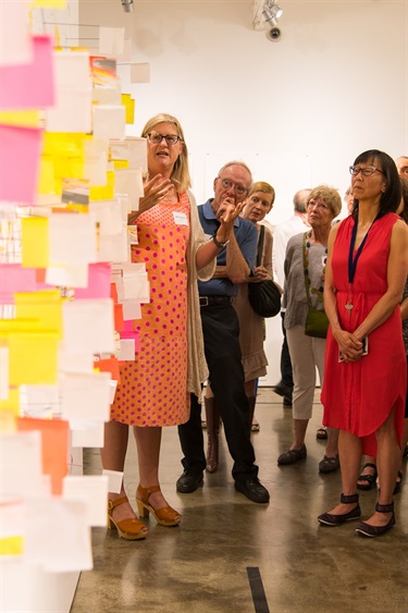 image of artist talking to group in front of paper installation