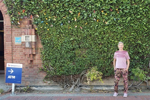 Artist standing in front of art installation of butterflies amongst the ivy covered brick wall