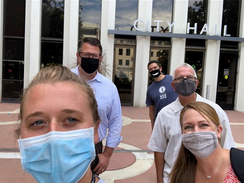 Several City Hall employees take a selfie in front of City Hall while wearing masks.