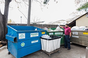Person placing clear bags of waste in refuse bins at Dinah's Hotel
