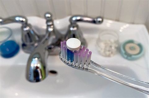 Toothbrush with toothpaste tablet, floss and mouthwash in background