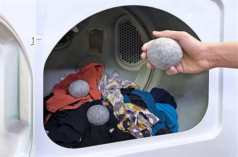 Wool dryer balls being placed into dryer with clothes