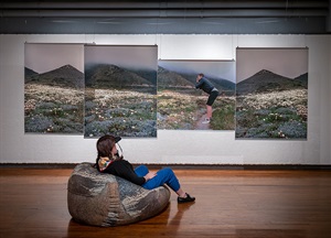a viewer reclines on a rock-like beanbag chair, observing photographs on the wall depicting a landscape